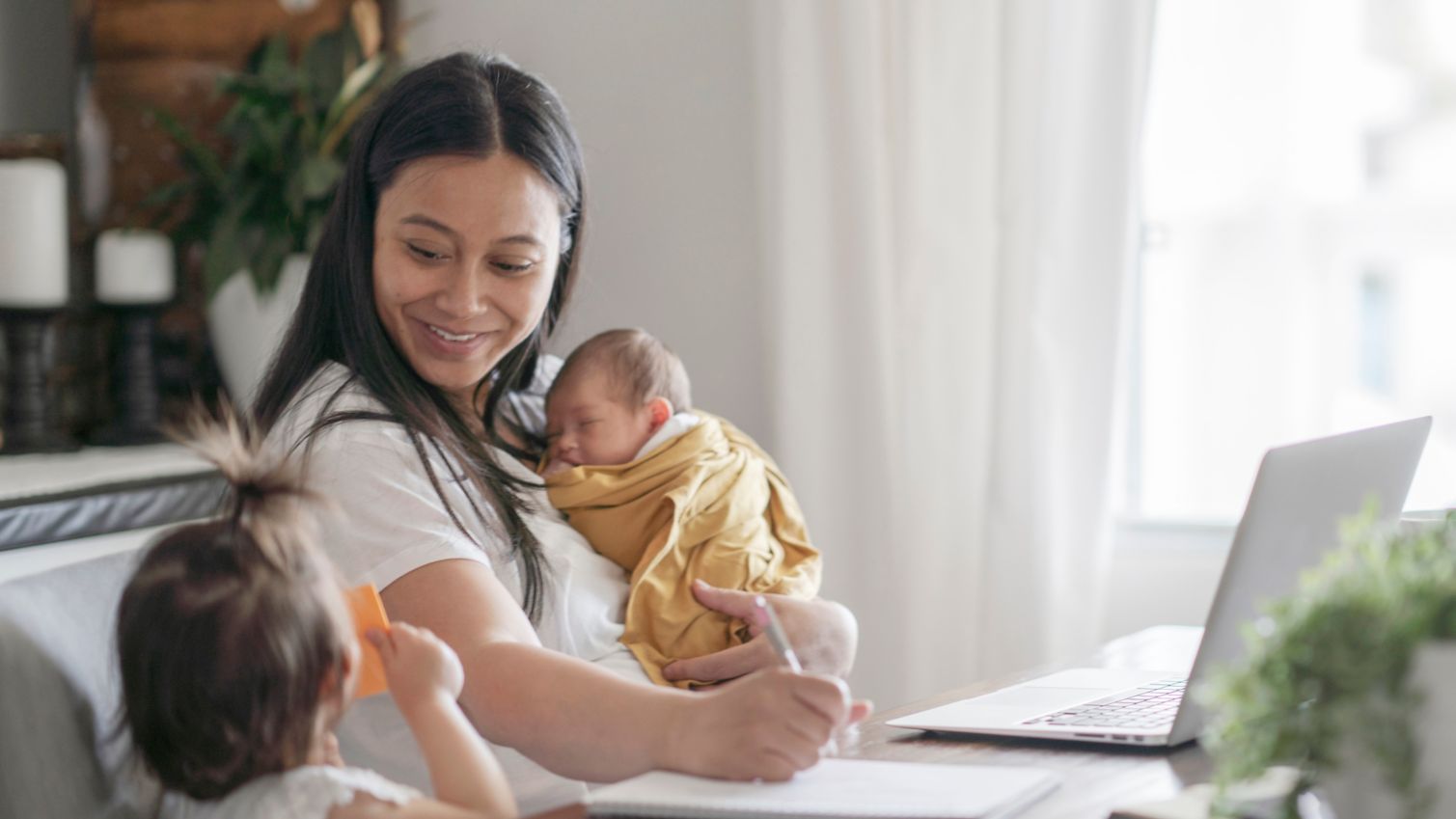 Mom holds infant next to toddler while filling out forms online